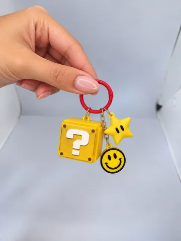 Llavero de bloque de interrogación con charms de estrella y carita feliz, en la mano