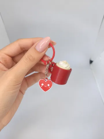 Llavero de taza con crema y charm de corazón, en la mano